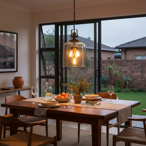 Satin brass pendant light with amber glass shades hanging over a dining table set with plates and glasses.