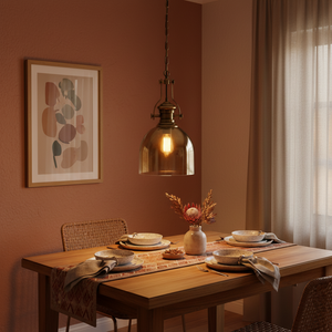 Satin brass pendant light hanging over a wooden dining table set with plates and a vase.