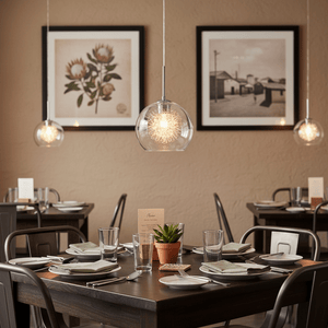 Polished chrome pendant light with clear glass shade hanging over a dining table set with plates and glasses.