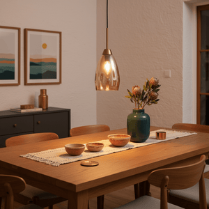 Gold and amber glass pendant light hanging above a wooden dining table with decorative bowls and flowers.
