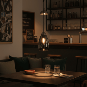 A stylish gun metal and smoke glass pendant light hanging over a dining table with glasses and a bowl.