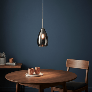 A sleek gun metal and smoke glass pendant light hanging above a wooden table with two cups.