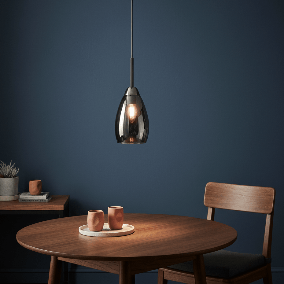 A sleek gun metal and smoke glass pendant light hanging above a wooden table with two cups.