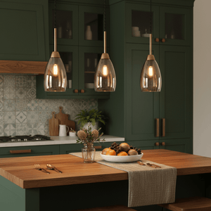 Three pendant lights with amber glass shades hang above a wooden kitchen island adorned with fruit.