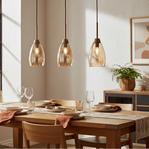 Three pendant lights with amber glass shades hang above a wooden dining table set with plates and glasses.