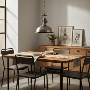 Satin chrome pendant light hanging over a wooden dining table set with plates and a table runner.