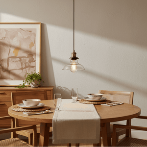 Antique brass pendant light with clear glass shade hanging above a wooden dining table set with dishes.