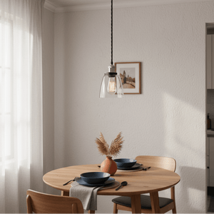 Satin chrome pendant light with clear glass shade hanging above a wooden dining table set with blue plates.