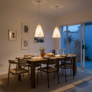 Two Tulip 3D Printed White Pendants hang over a wooden dining table set for a meal, creating a warm ambiance.