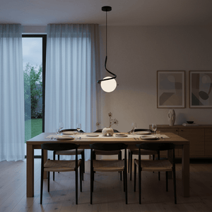 Modern black pendant light hanging above a wooden dining table set for a meal, with soft curtains in the background.
