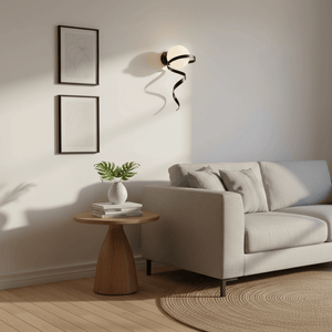 Black Infinity Wall Light mounted beside a couch, casting soft shadows on the wall, with framed art and a decorative table.