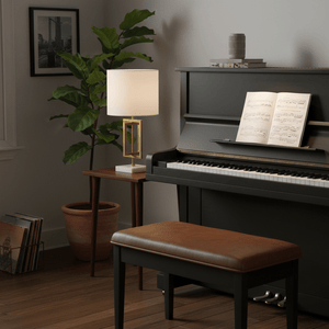 Chopin Gold & Marble Table Lamp on a side table beside a piano, with sheet music and a plant in the background.
