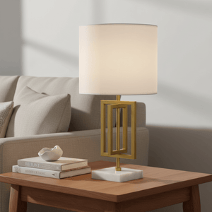 Chopin Gold & Marble Table Lamp on a wooden side table next to a beige sofa, with books and a decorative dish.