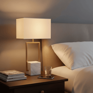 Verdi Gold & Marble Table Lamp on a bedside table, illuminating a cozy bedroom scene with books and a glass.