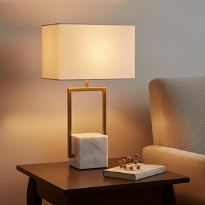 Verdi Gold & Marble Table Lamp on a wooden side table, with a soft fabric shade and marble base, beside a cozy sofa.