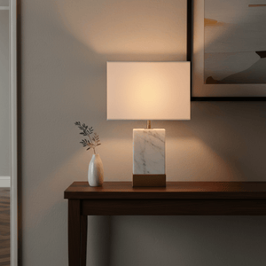 Bach Gold & Marble Table Lamp on a wooden console table with a small vase and artwork in the background.