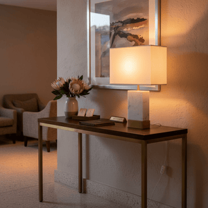 Bach Gold & Marble Table Lamp on a console table with flowers and artwork in the background.