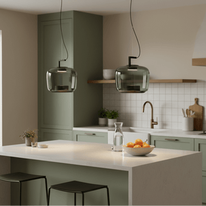 Two green-tinted LED pendant lights hang over a kitchen island with a bowl of oranges and a water carafe.