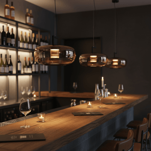 Three amber glass pendant lights with warm white LED lighting hang over a wooden bar counter in a dimly lit bar setting.