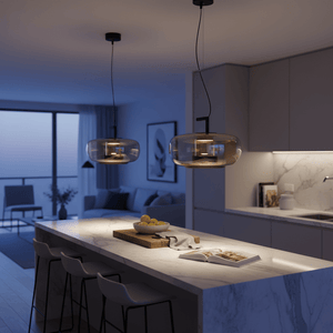 Two amber glass pendant lights hang above a marble kitchen island, illuminating a bowl of lemons and an open book.