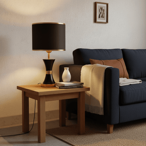 Efron Black & Gold Table Lamp on a wooden side table beside a dark sofa, with books and a vase.