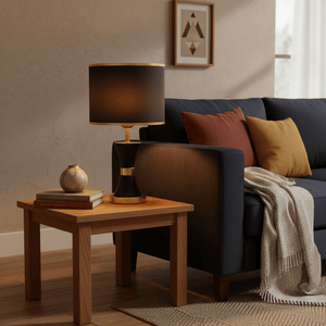 Efron Black & Gold Table Lamp on a wooden side table beside a dark sofa with decorative pillows.