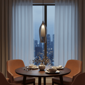 A black smoke pendant light hangs above a round wooden table set with dishes, glasses, and a small plant.