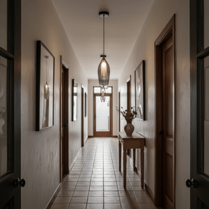 A black smoke pendant light hangs from the ceiling in a hallway with wooden doors and framed artwork on the walls.