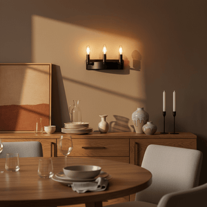 A black three-light wall fixture mounted on a beige wall, casting warm light over a wooden sideboard with decorative items.