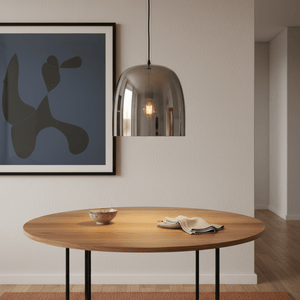 Smoke-tinted dome pendant light hanging over a wooden dining table with a decorative bowl and cloth.