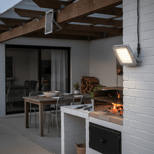 Karu 50W LED Solar Floodlight mounted on a wall, illuminating a braai area with a table and chairs in the background.