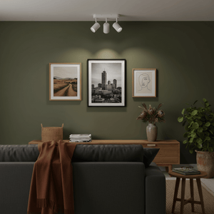 Three-light adjustable spotlight mounted on a green wall, illuminating framed artwork above a sofa.