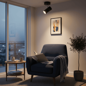 Adjustable matt black ceiling spotlight illuminating a cozy reading nook with a blue armchair and side table.