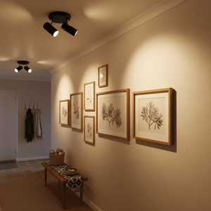Two adjustable black ceiling spotlights illuminating framed artwork on a wall in a cozy hallway.