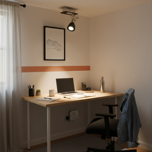 A polished chrome and black spotlight illuminating a modern desk setup with a laptop and stationery.