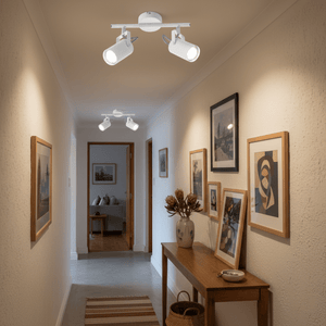 A modern 2-light white ceiling spotlight installed in a hallway, illuminating framed artwork on the walls.