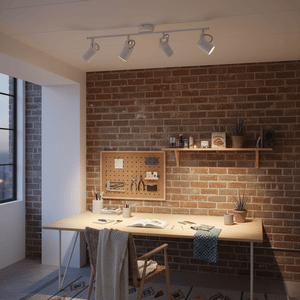 Ceiling spotlight illuminating a modern workspace with a wooden desk and brick wall.