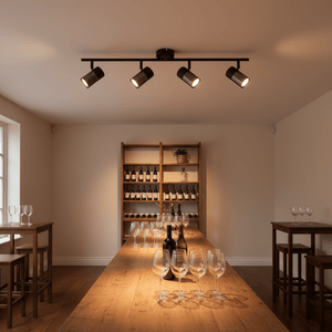 Black 4-light spotlight with moveable arms illuminating a wooden table set with glasses and wine bottles.