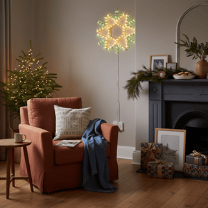 Indoor scene featuring a snowflake motif LED light above a cozy armchair with a festive tree and decorations.