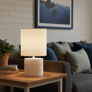 Valencia White Table Lamp on a wooden side table, illuminating a cozy living room with green cushions.