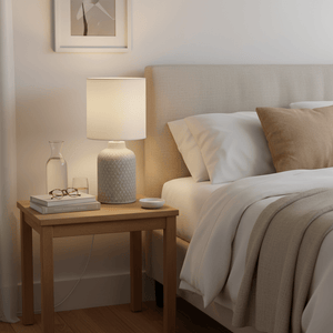 A stylish table lamp on a bedside table, surrounded by a water carafe, glasses, and books, creating a cozy atmosphere.