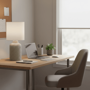 A stylish ceramic table lamp on a wooden desk, illuminating a laptop and stationery in a bright office setting.