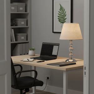 A stylish table lamp with a hessian shade on a desk beside a laptop and stationery, creating a warm workspace.