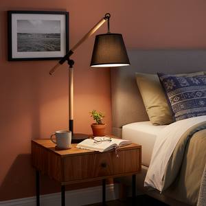 A modern black and wood table lamp on a bedside table, illuminating a cozy bedroom scene with a book and plant.