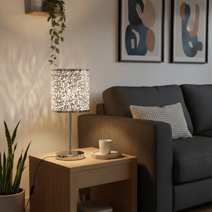Polished chrome table lamp with a silver patterned shade on a wooden side table next to a grey couch.