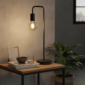 Sleek black metal table lamp on a wooden side table with magazines, a glass, and a plant.