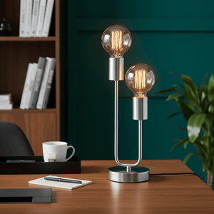 Hensel Satin Chrome Table Lamp with two bulbs on a wooden desk, surrounded by books and a plant.