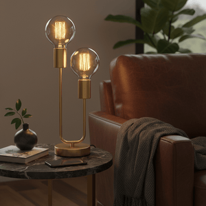 Hensel Brass Table Lamp on a marble side table next to a brown leather chair, with warm light bulbs and a plant.