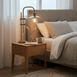 Finique Brass Table Lamp on a wooden nightstand beside a bed, featuring a warm brass finish and adjustable head.