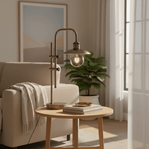 Finique Brass Table Lamp on a wooden side table beside a beige sofa, with a plant in the background.